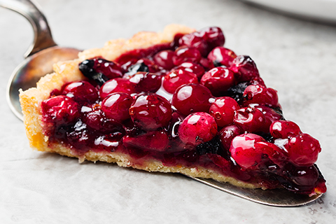 Tart, pie, cake with jellied fresh cranberries, bilberries and winter spices on a grey stone background.