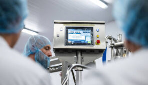 Food production technicians monitoring automated food processing equipment in a hygienic manufacturing facility.