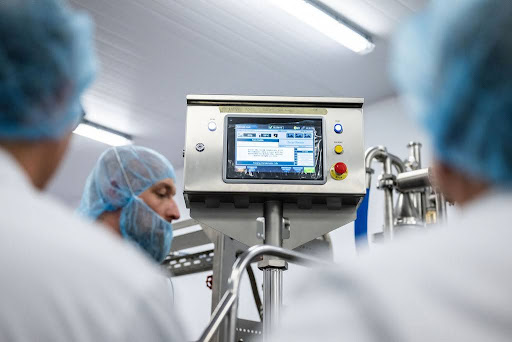 Food production technicians monitoring automated food processing equipment in a hygienic manufacturing facility.