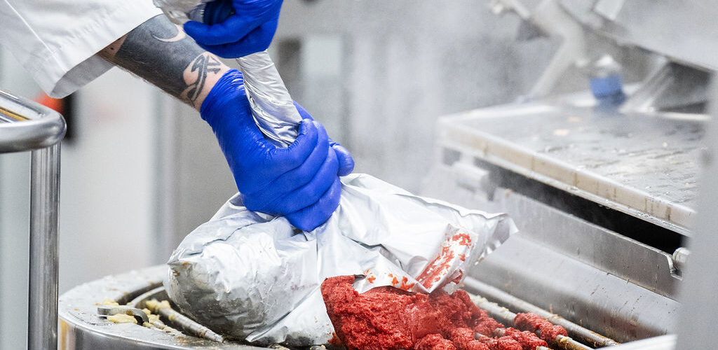 Food production worker operating industrial cooking systems in a commercial processing facility.