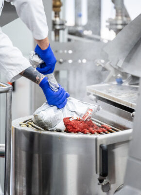 Food production worker operating industrial cooking systems in a commercial processing facility.