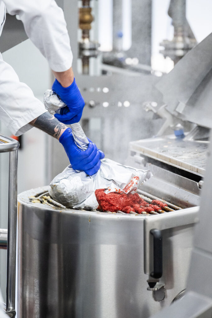 Food production worker operating industrial cooking systems in a commercial processing facility.
